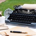 Vintage black typewriter with old books and flowers on wooden t